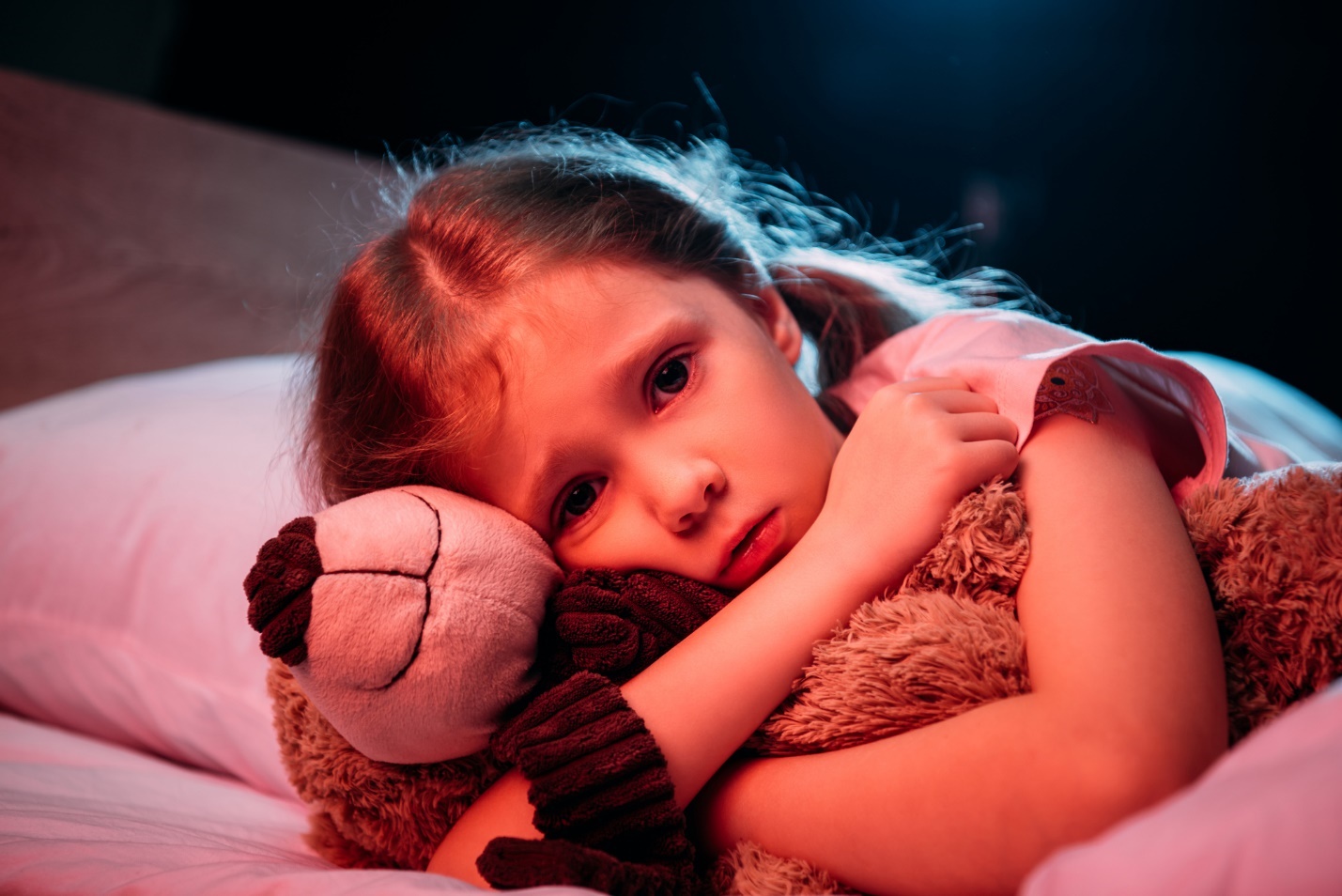 A child lays on a bed with a teddy bear

Description automatically generated with medium confidence