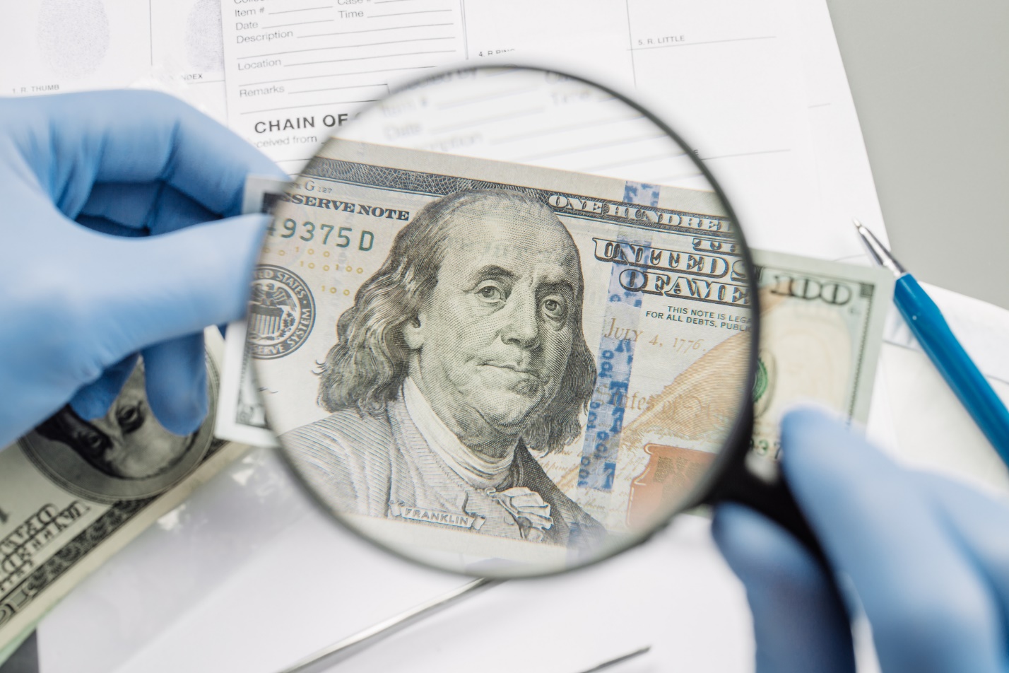 A person holding a magnifying glass looking at a dollar bill

Description automatically generated