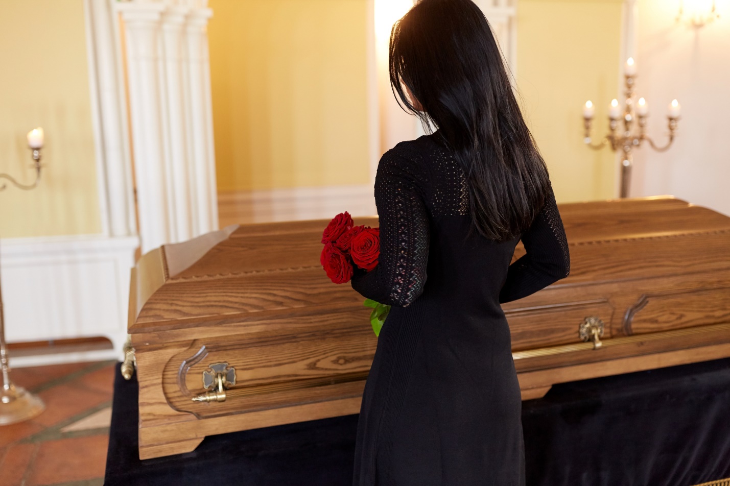 A person holding flowers standing in front of a coffin

Description automatically generated