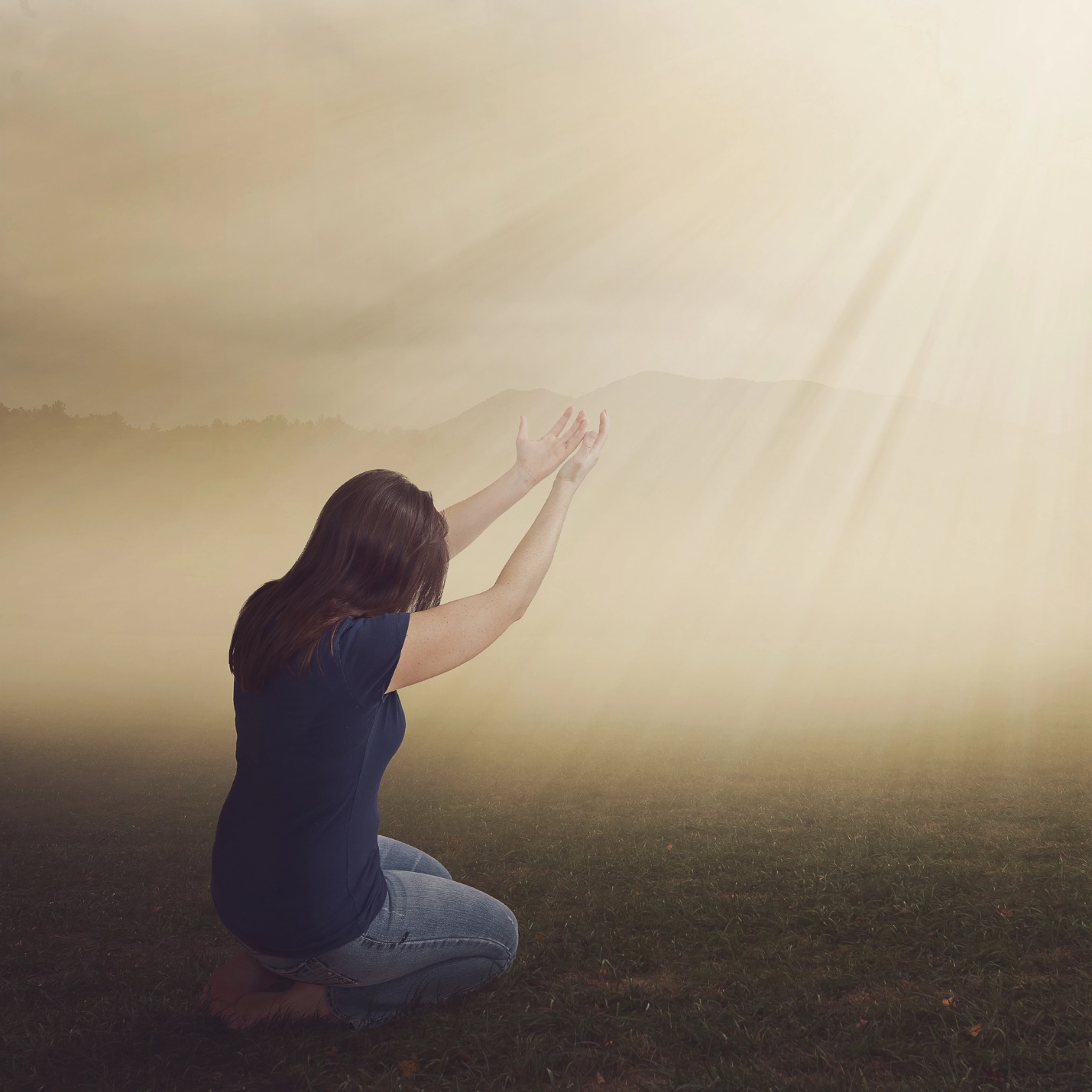 A person kneeling in the grass with her hands raised

Description automatically generated
