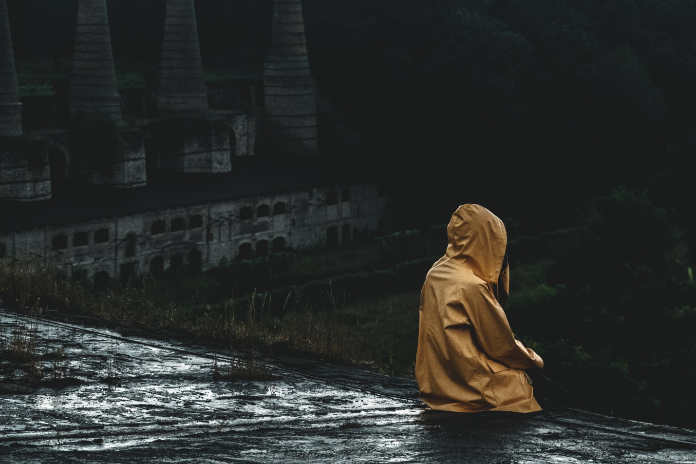 A person in a raincoat sitting on a wet surface

Description automatically generated