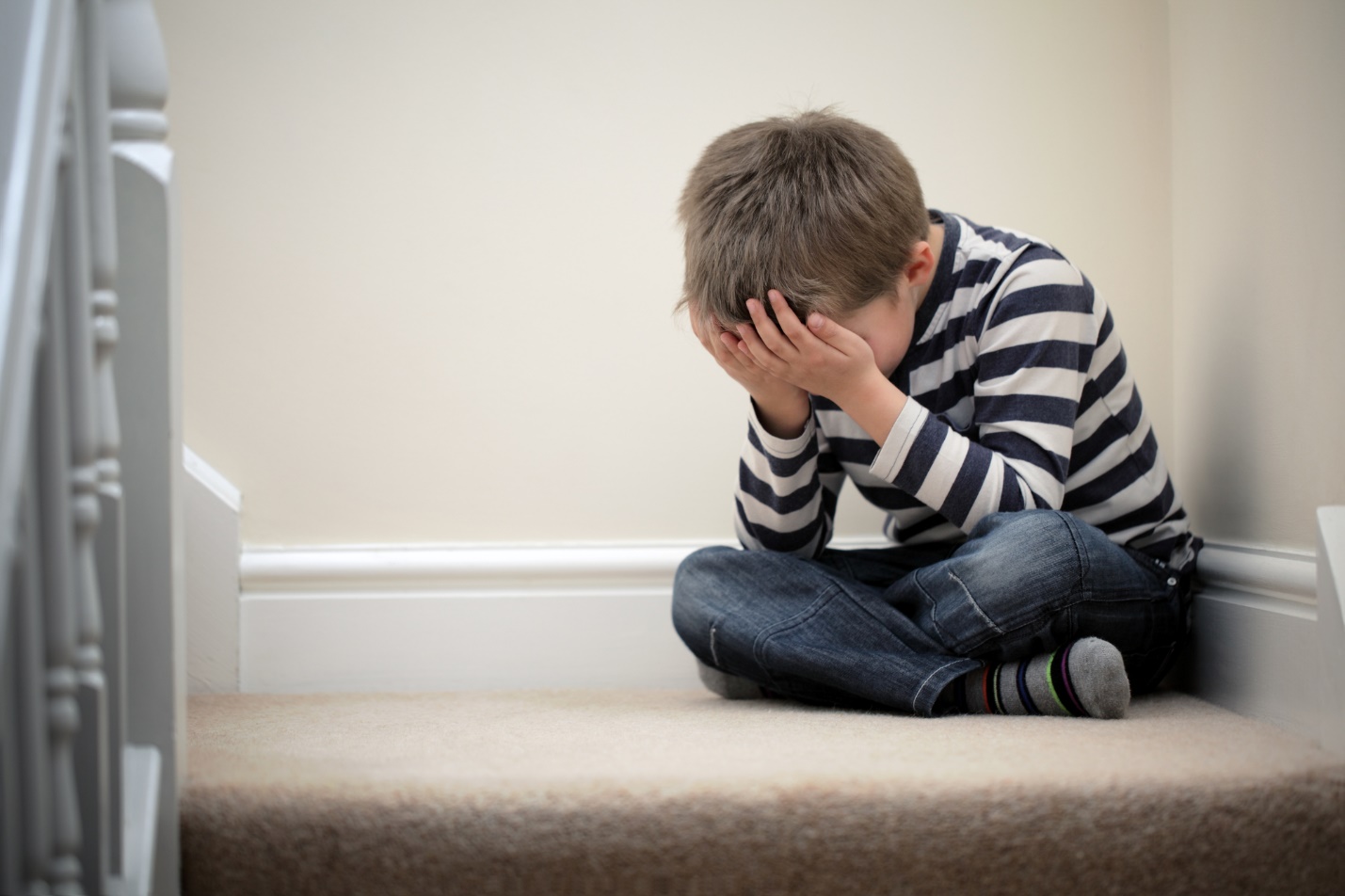 A child sitting on the floor with his hands in his face

Description automatically generated