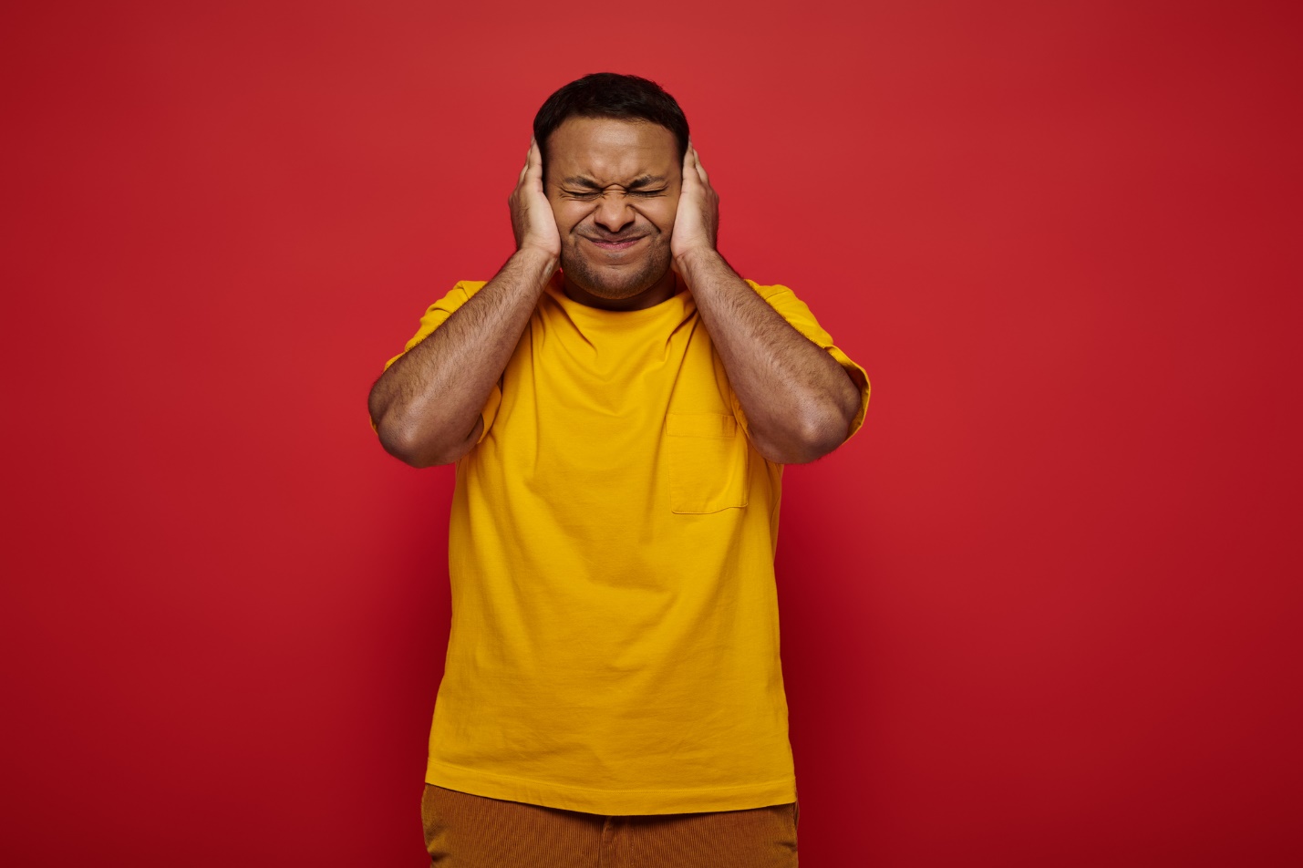 A person in a yellow shirt covering his ears with his hands

Description automatically generated