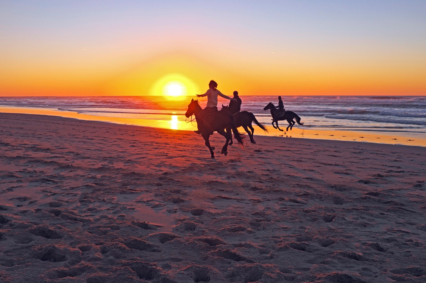 People riding horses on a beach

Description automatically generated