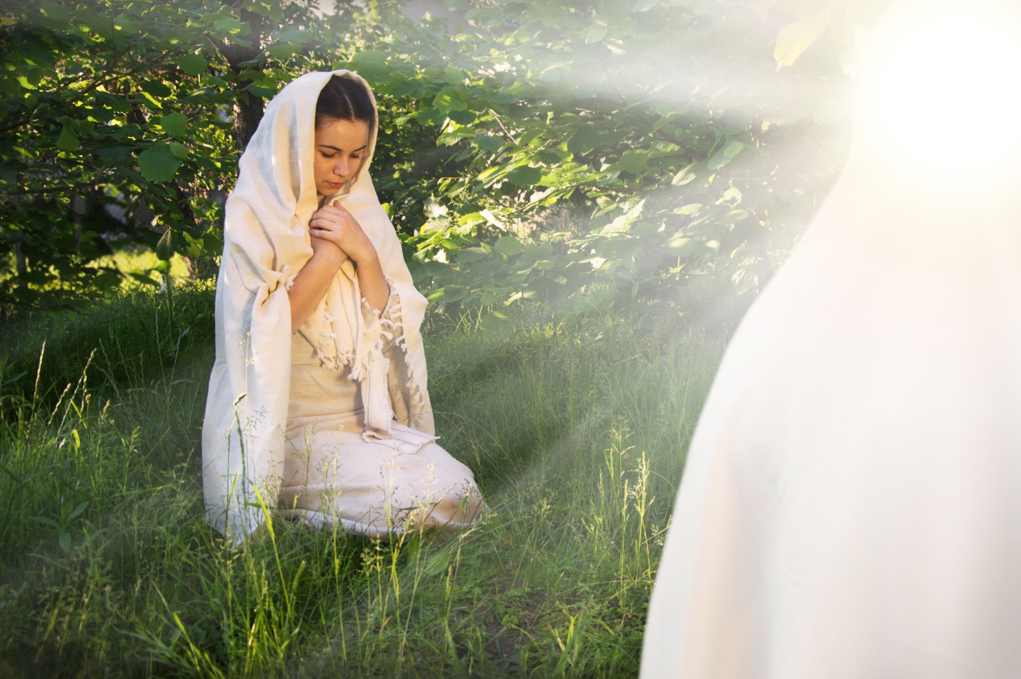 A person kneeling in the grass with her hands folded

Description automatically generated