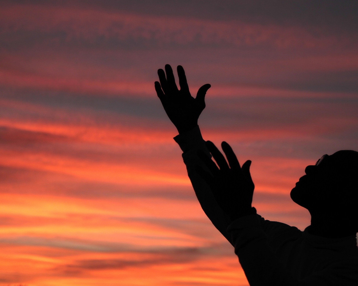 A silhouette of a person with her hands raised

Description automatically generated