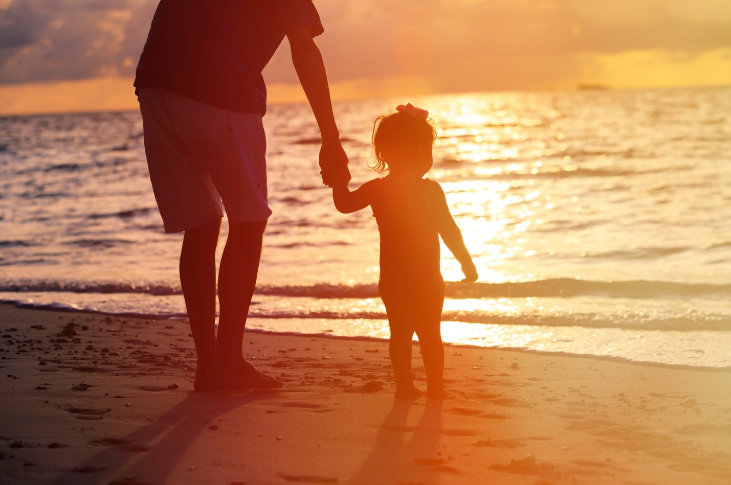 A person and child holding hands on a beach

Description automatically generated