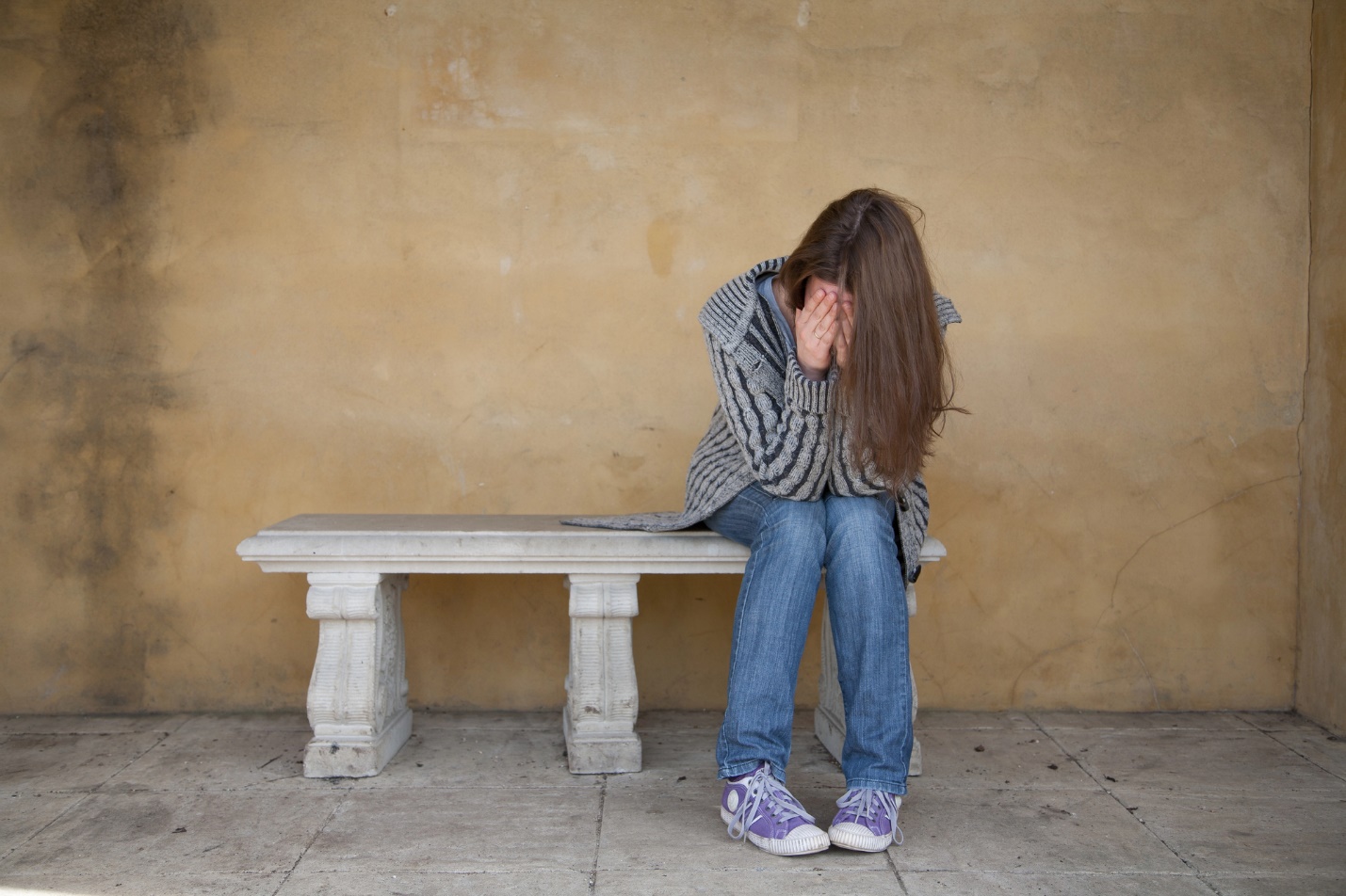 A person sitting on a bench covering her face

Description automatically generated