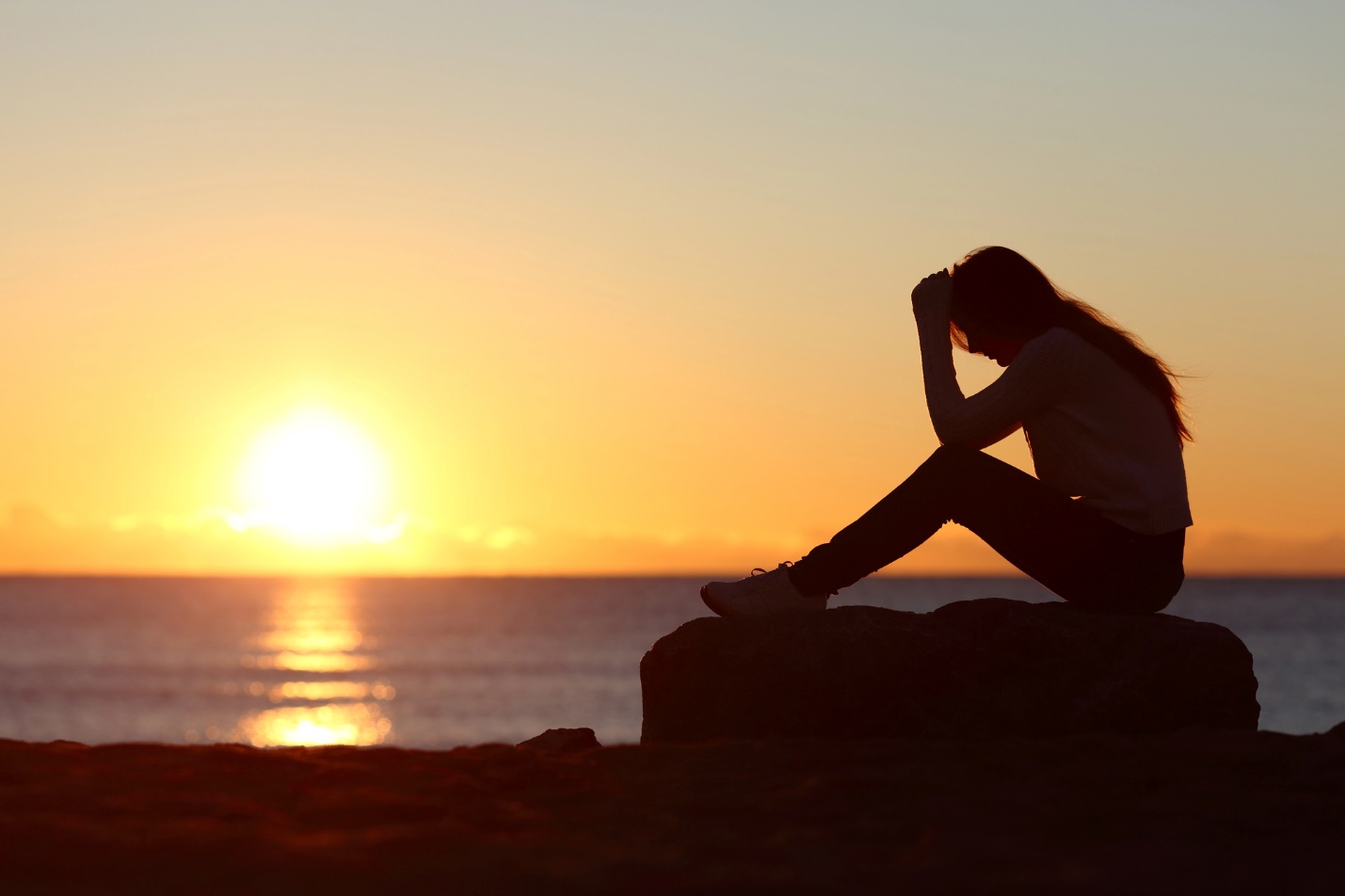 A person sitting on a rock with her hands on her head

Description automatically generated