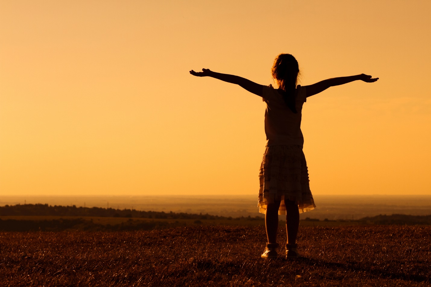 A silhouette of a child with her arms out in the air

Description automatically generated