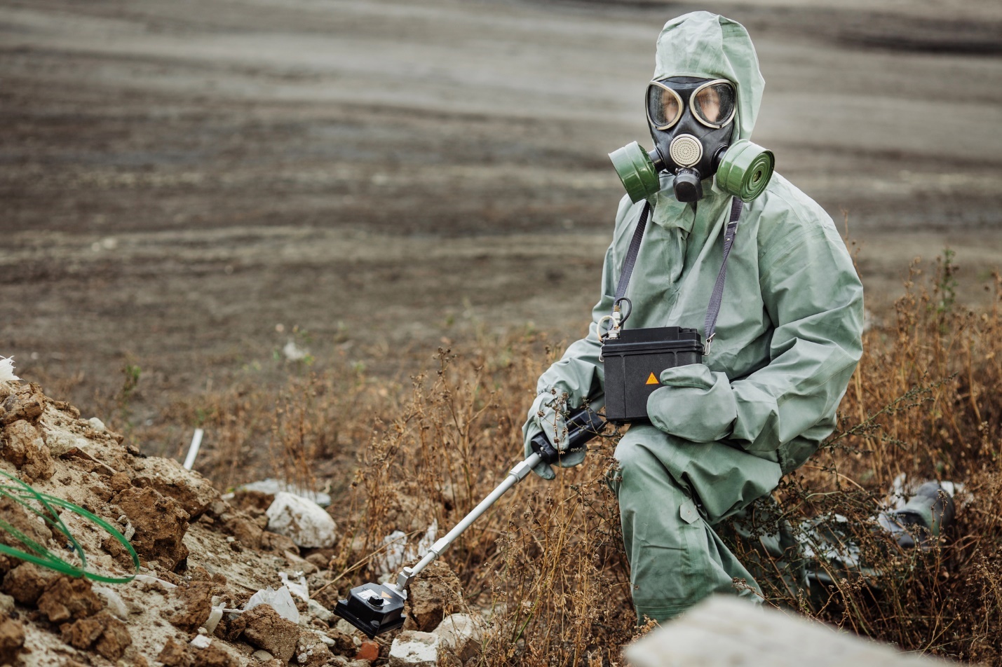 A person in a gas mask and gas mask sitting in a dirt area

Description automatically generated