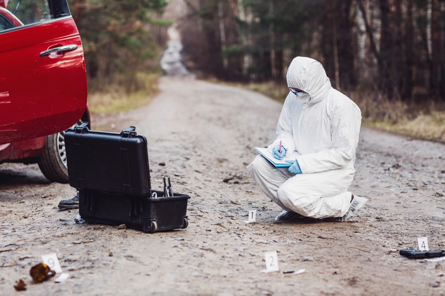 A person in white protective suit kneeling on dirt with a computer

Description automatically generated