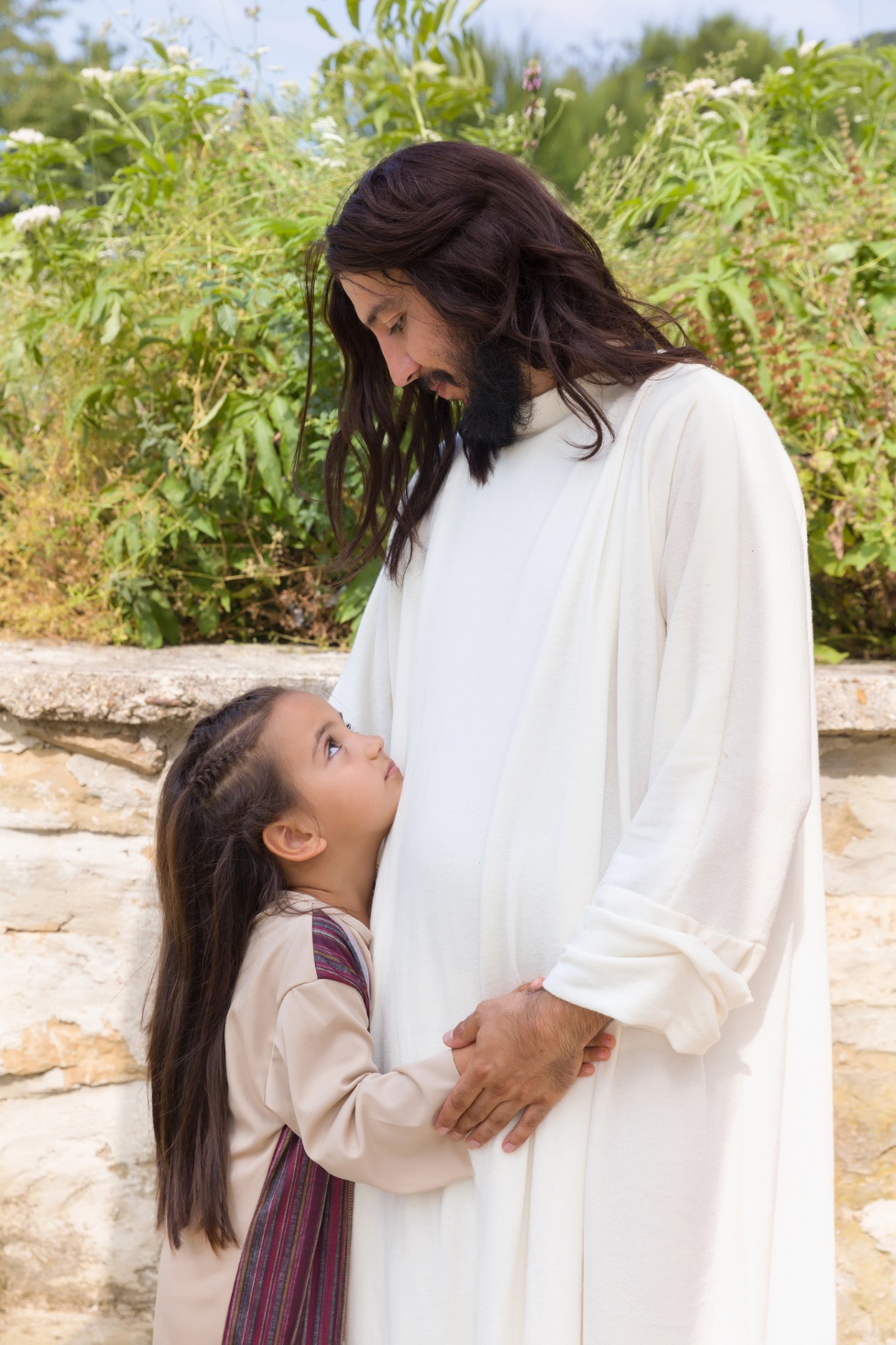 A person in white robe holding a child's belly

Description automatically generated