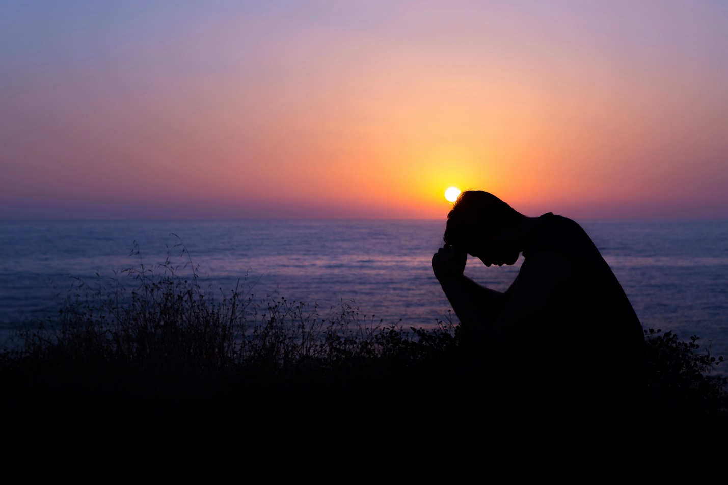 A silhouette of a person sitting on a hill with the sun setting behind him

Description automatically generated